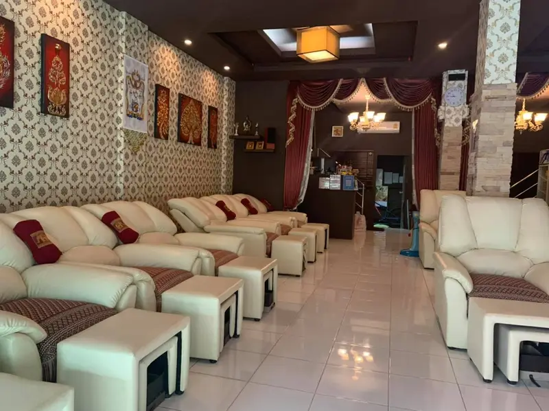 The foot massage lounge: rows of cream reclining armchairs with burgundy Thai-weave cushions and footstools, damask wallpaper and gold Thai artwork